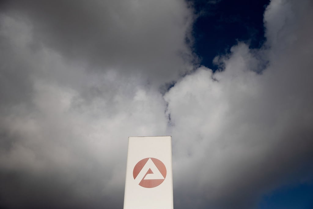 Wolken ziehen über ein Schild der Agentur für Arbeit.