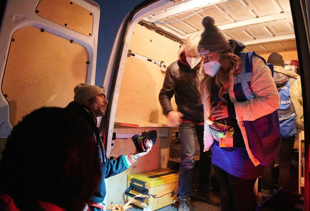 Kathy und Matthias geben einem Obdachlosen (l) ein paar Handschuhe.