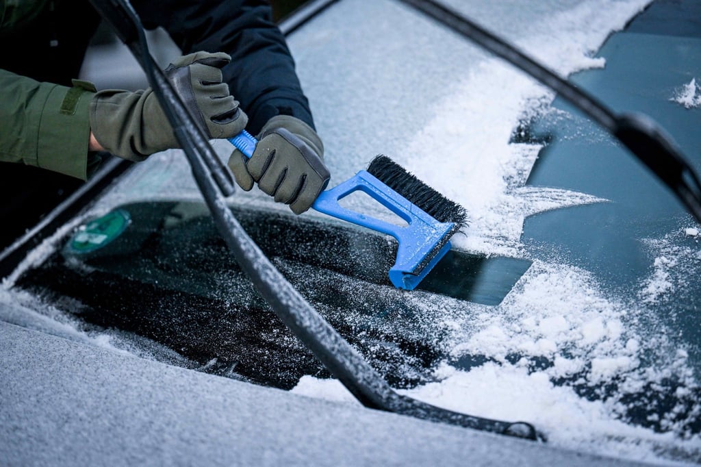 Ein Fahrer muss unter Kraftanstrengung mit dem Eiskratzer die Frontscheibe seines PKW vom Eis befreien.