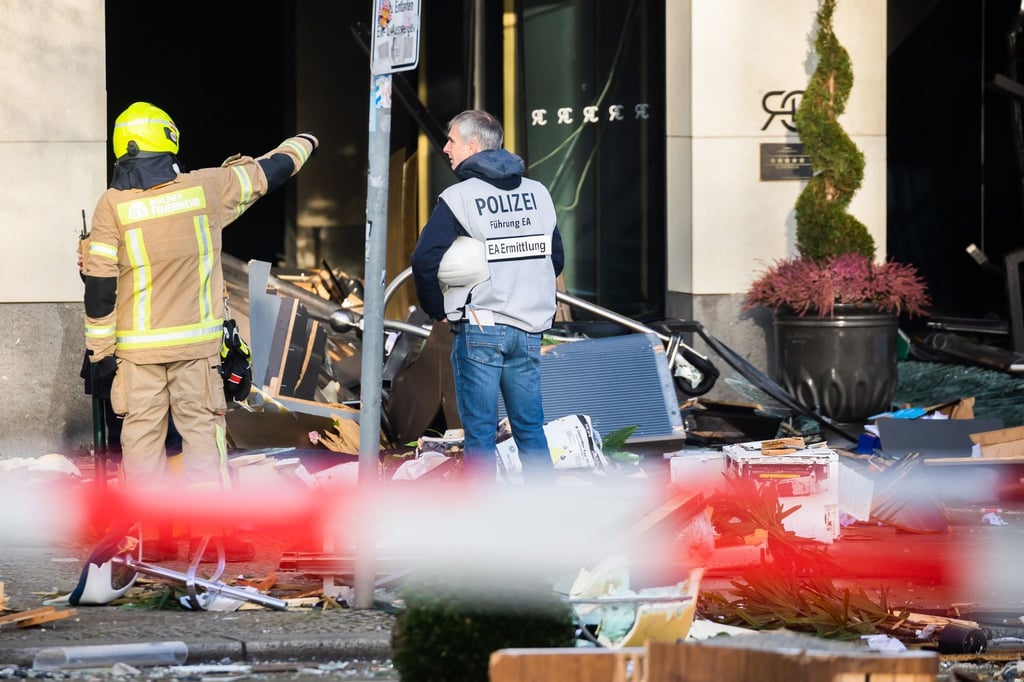 Ein Polizeibeamter begutachtet neben einem Feuerwehrmann auf der Karl-Liebknecht-Straße Trümmer vor einem Hotel.