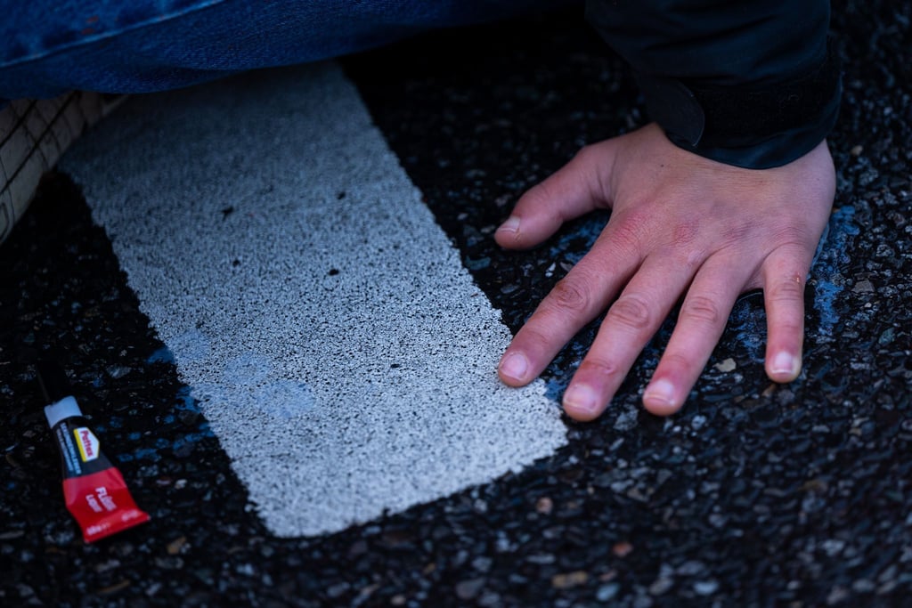 Ein Klimaaktivist der Umweltschutzbewegung „Letzte Generation“ klebt mit der Hand auf einer Straße.