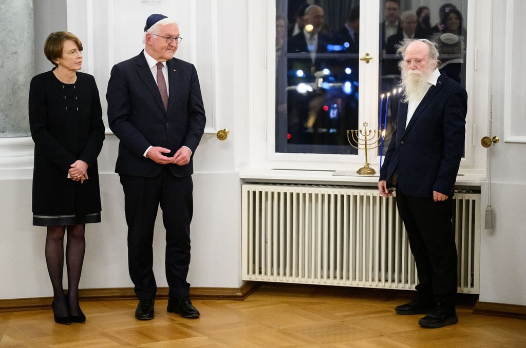 Bundespräsident Frank-Walter Steinmeier und seine Frau Elke Büdenbender sowie Yehuda Mansbach (r), der Enkel von Rabbiner Arthur Posner, bei der gemeinsamen Chanukka-Feier im Schloss Bellevue. Auf der Fensterbank steht der Chanukka-Leuchter der Familie Posner.