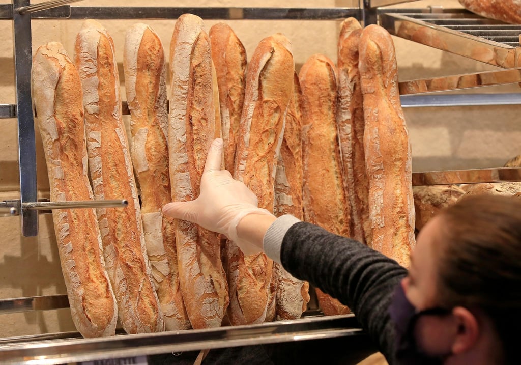 Ein Verkäuferin nimmt ein Baguette aus dem Regal einer Bäckerei.