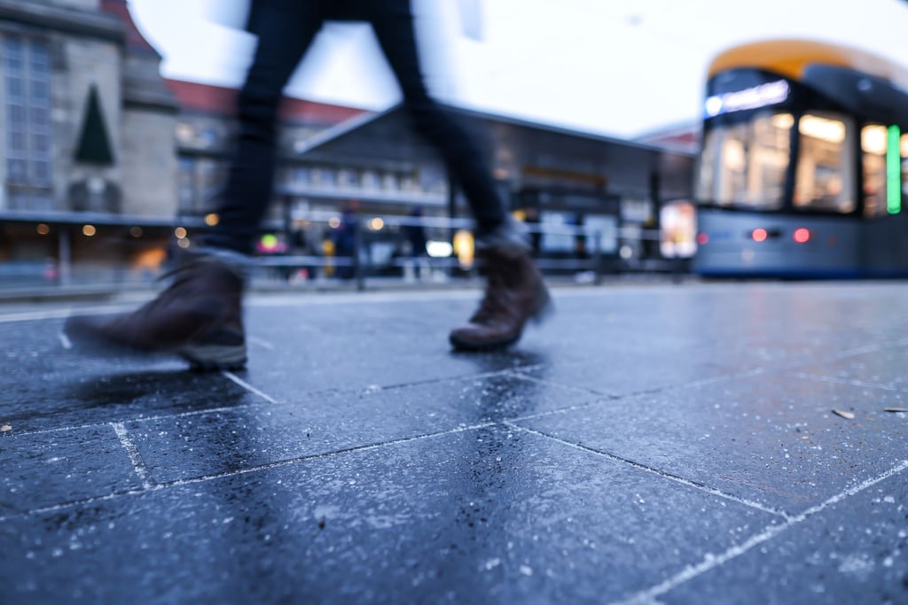 Eine Passantin geht über die feuchte Haltestelle vor dem Leipziger Hauptbahnhof.
