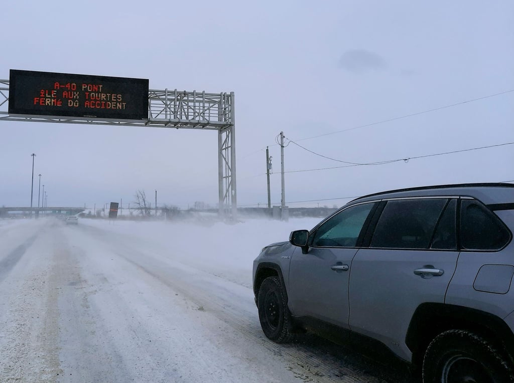 Kältwelle in Kanada: Ein Auto fährt auf der schneebedeckten Ile aux Tourtes-Brücke, die von Ontario nach Montreal führt, während eine Anzeige eine Vollsperrung aufgrund eines wetterbedingten Unfalls anzeigt.
