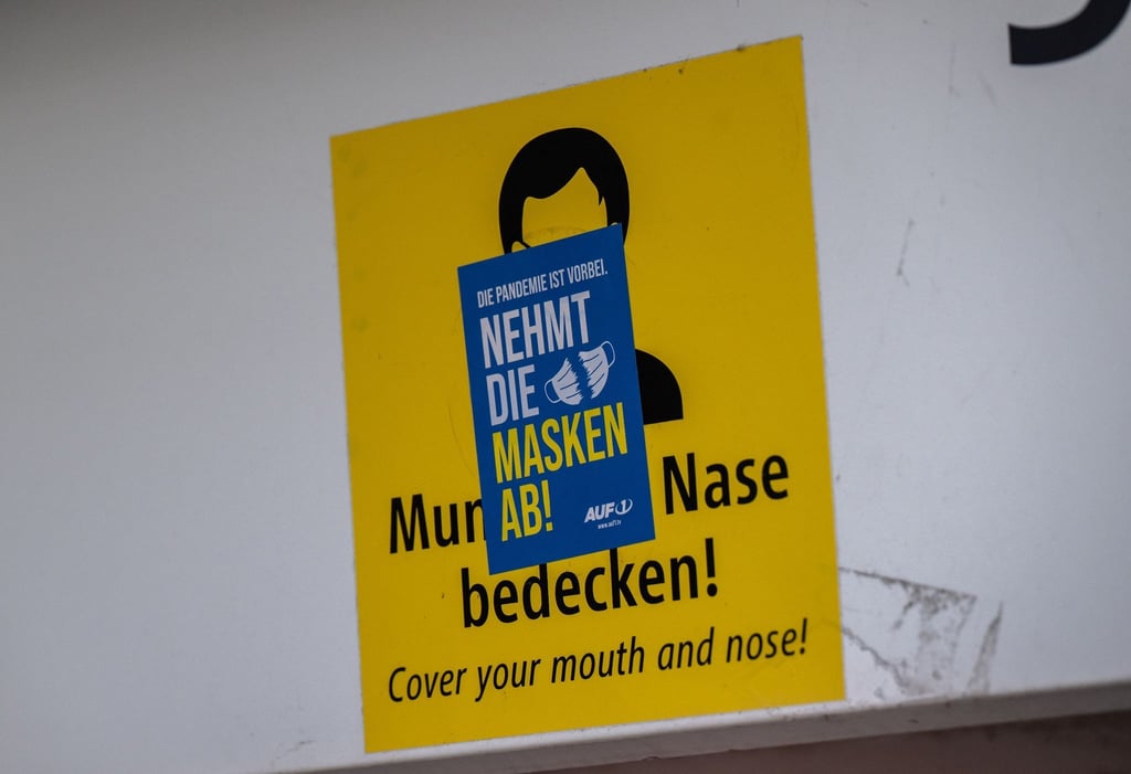 Ein Aufkleber mit der Aufschrift „Nehmt die Masken ab!“ klebt über einem Schild, das zum Tragen einer Mund-Nasen-Maske auffordert. Die Mehrheit der Deutschen ist einer neuen Umfrage zufolge weiter für eine Isolationspflicht für Corona-Infizierte.