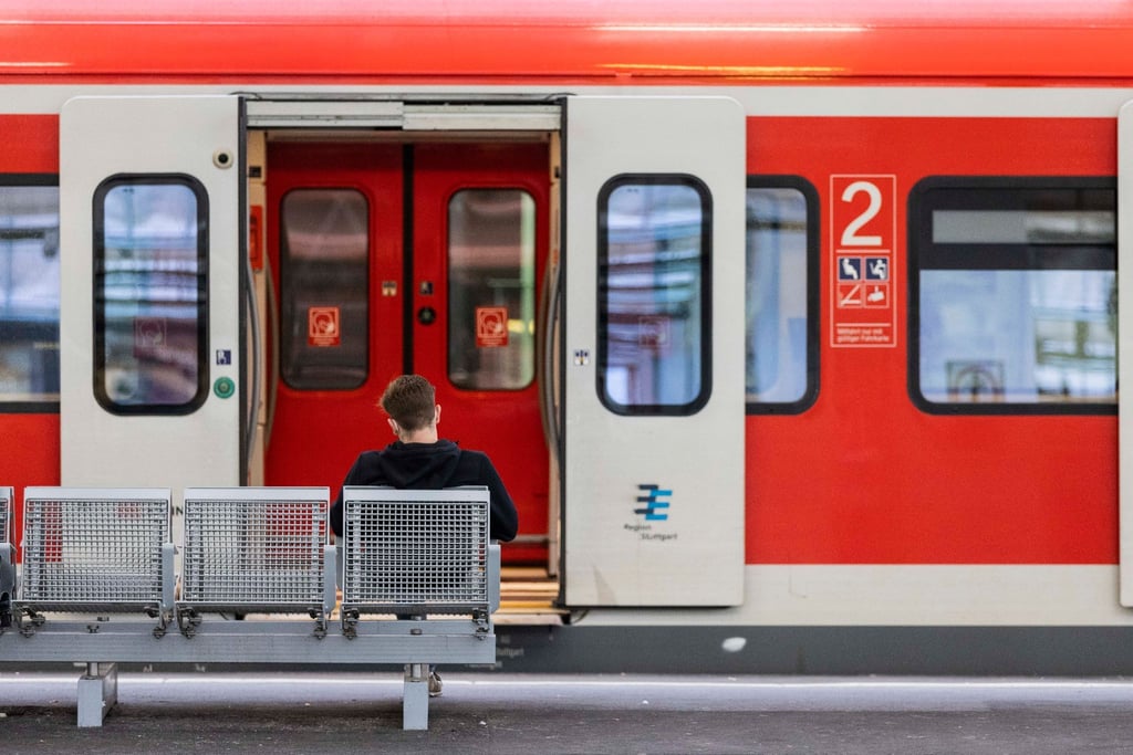 Ein Mann sitzt an einem Bahnhof vor einem Regionalzug auf der Bank.