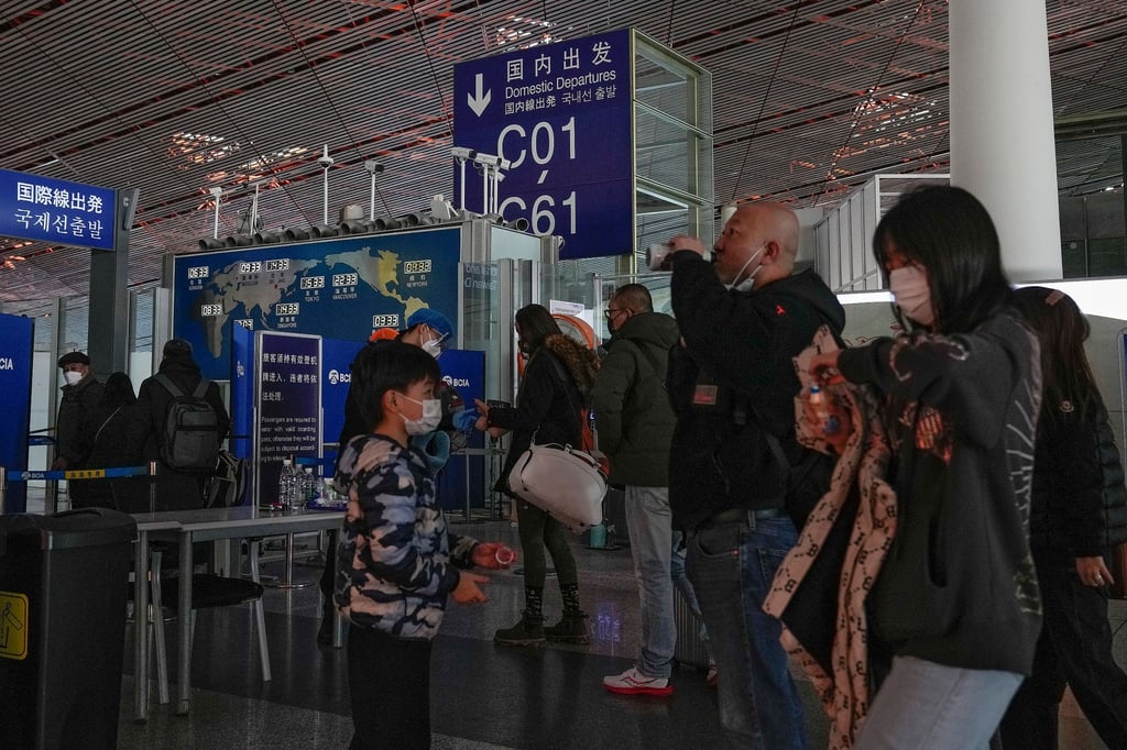 Passagiere mit Mund-Nasen-Schutz stehen am Flughafen Peking an der Sicherheitskontrolle vor einem internationalen Abfluggate an.