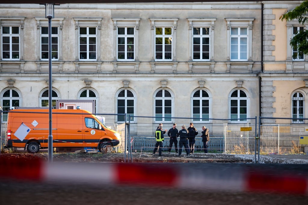 Mitglieder von Polizei, Kampfmittelräumdienst und Feuerwehr stehen hinter der Absperrung an einer Baustelle.