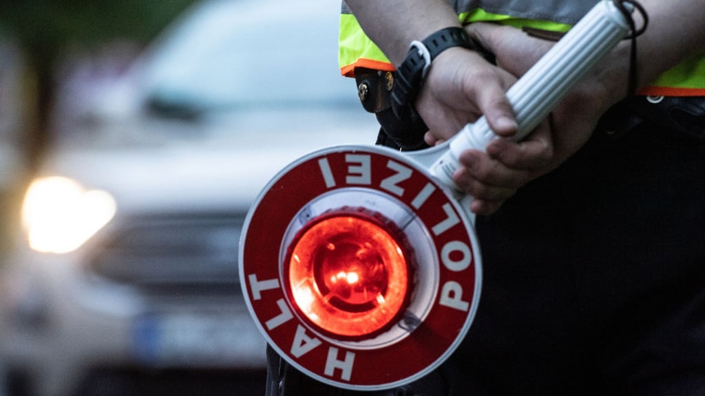 Ein Polizist hält bei einer Verkehrskontrolle eine Winkerkelle in der Hand.