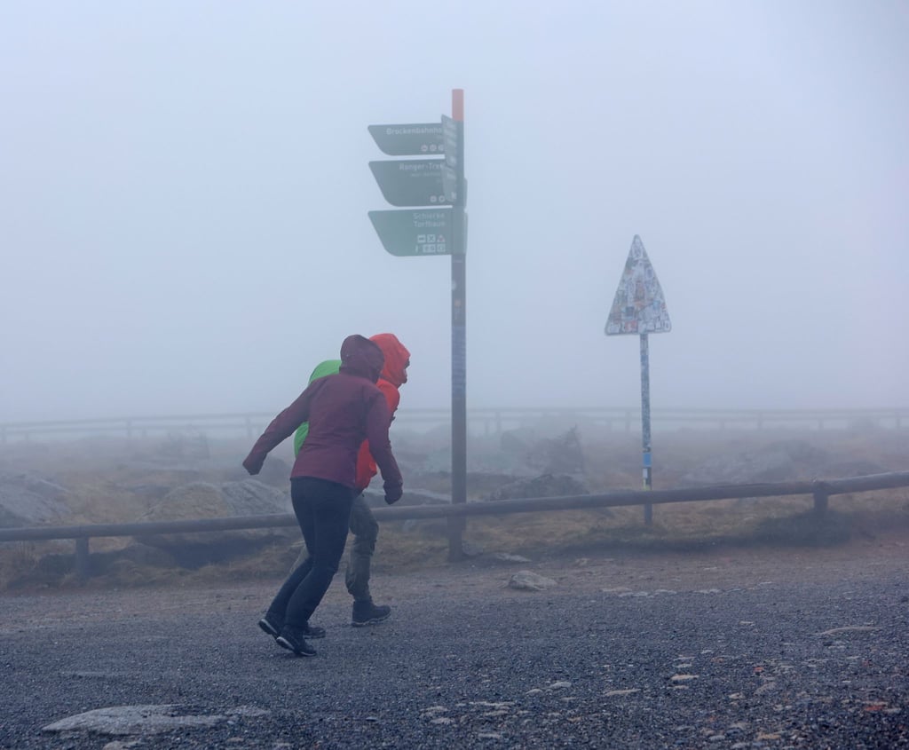Wanderer stemmen sich auf dem Brocken gegen den Wind.