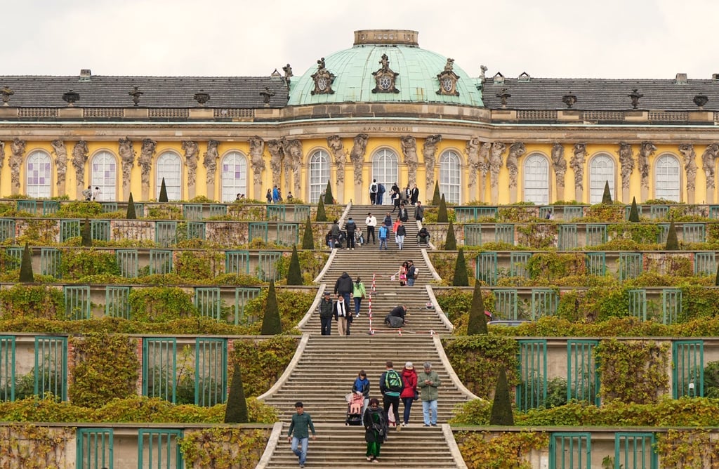 Touristen gehen bei sonnigem Wetter auf der Treppe zum Schloss Sanssouci.