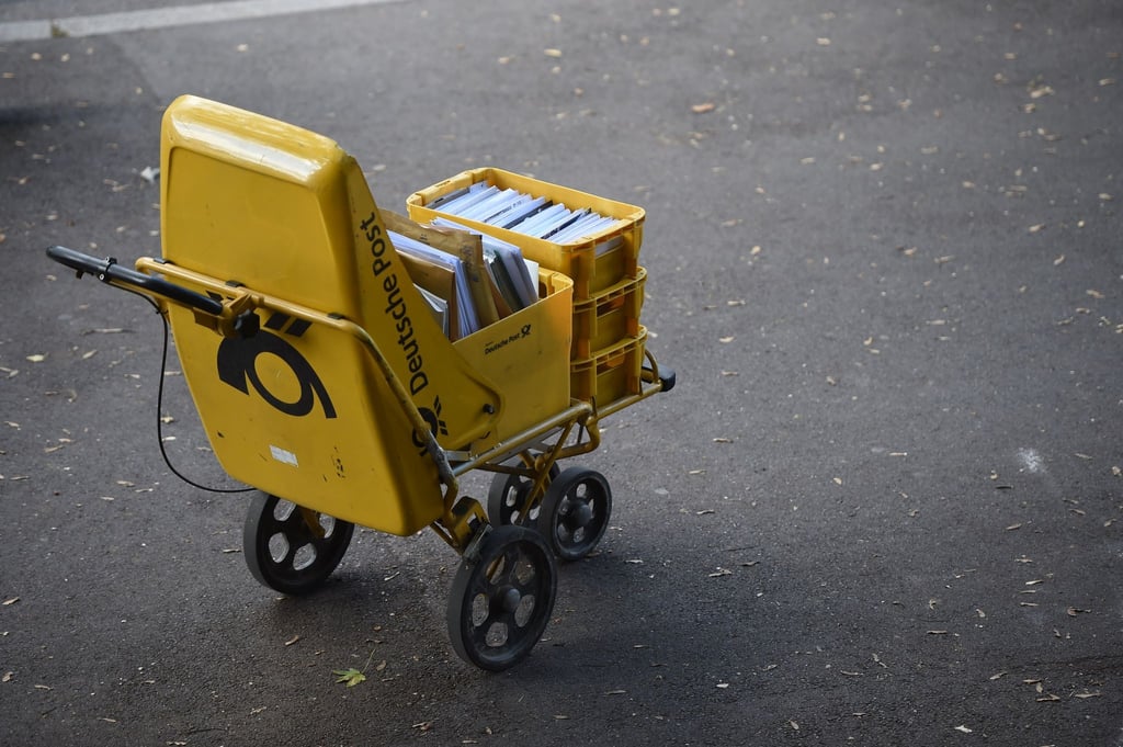 Ein Trolley eines Zustellers der Deutschen Post steht auf der Straße.