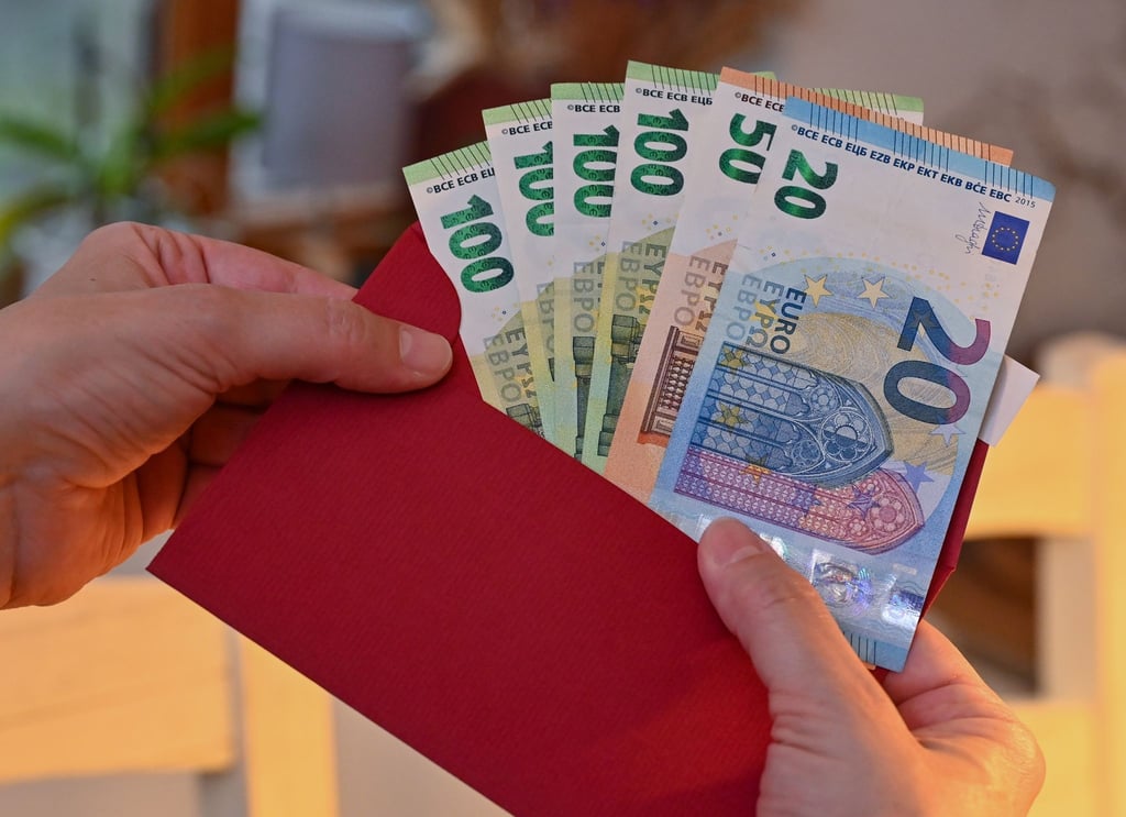 Eine Frau steckt Eurobanknoten in einen Umschlag.