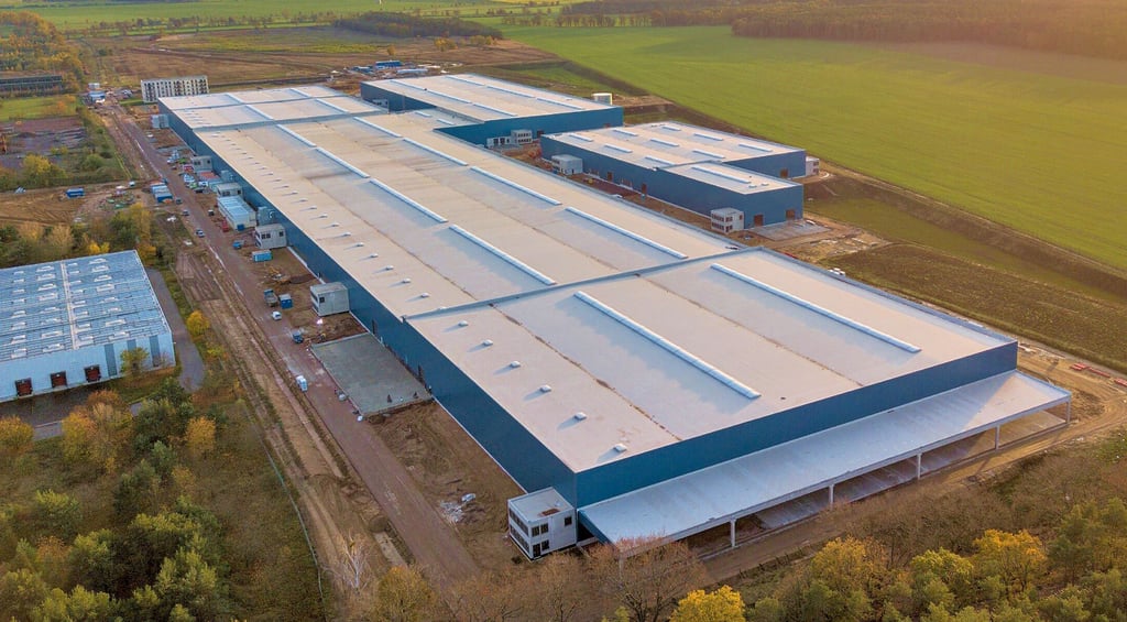 Die Giga-Factory Stegelitz aus der Luft. Das hinten links an der Fabrikhalle angrenzende Gebäude ist ein fünfstöckiges Wohnhaus, wie es künftig hier in der Nokera-Fabrik vorgefertigt werden soll.