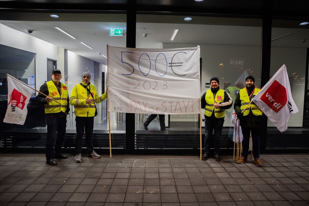 Teilnehmer eines Warnstreiks am Flughafen Berlin-Brandenburg BER halten ein Banner mit der Aufschrift „500€, 2023“.