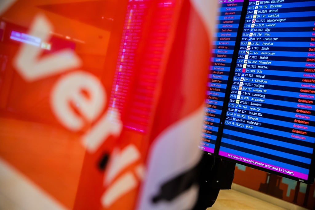 Eine Verdi-Fahne ist während eines Warnstreiks am Flughafen Berlin-Brandenburg BER vor einer Anzeigetafel zu sehen.