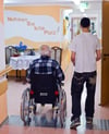 Im einem Seniorenheim betreut ein junger Mann einen Mann im Rollstuhl.