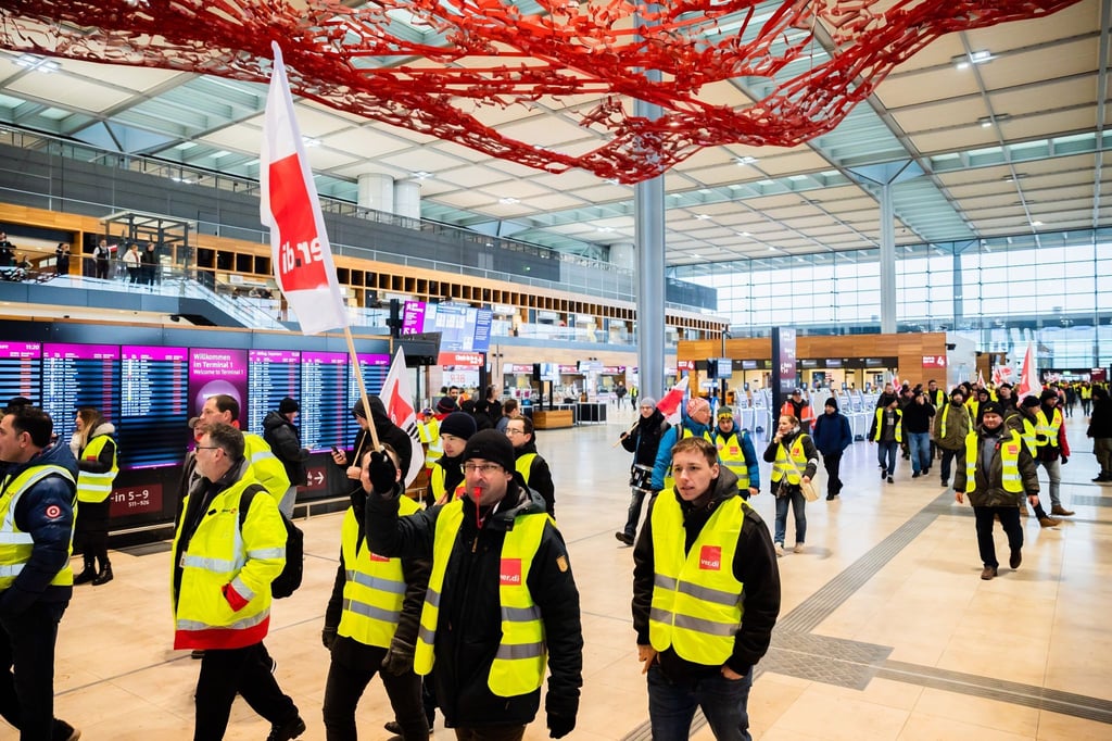 Teilnehmer einer Demonstration zum Warnstreik am Flughafen Berlin-Brandenburg BER laufen durch das Terminal 1.