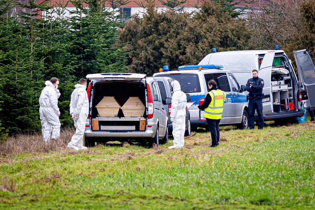 Mitarbeiter der Spurensicherung der Polizei stehen an einem Leichenwagen.