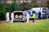 Mitarbeiter der Spurensicherung der Polizei stehen an einem Leichenwagen.