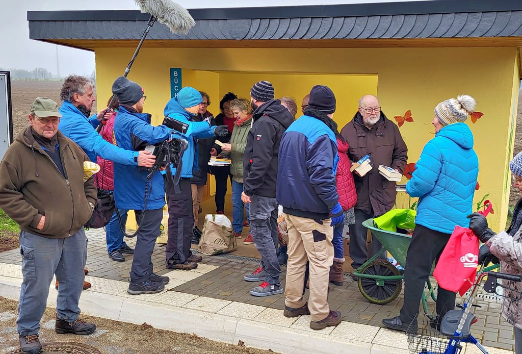 Reporter Michael Wasian (Mitte) spricht nach der Ankunft an der Bushaltestelle in Quellendorf mit Diesdorfern, die die Bücher in den Schrank einräumen.