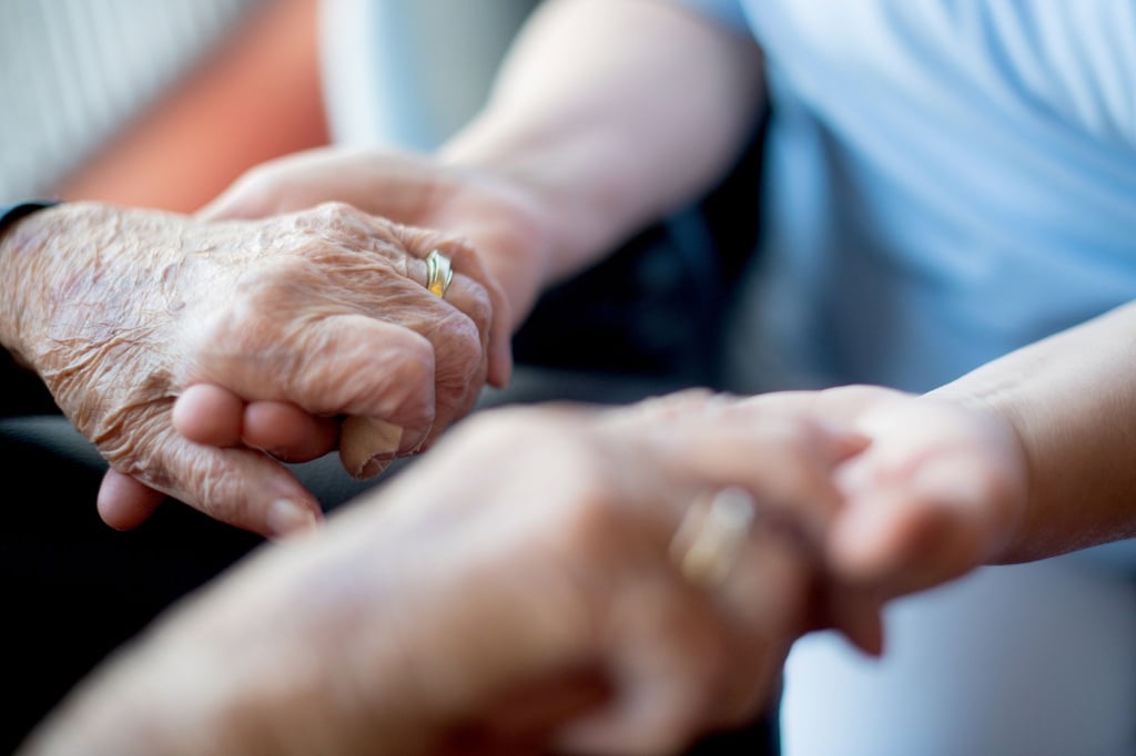 Eine Pflegerin hält die Hände einer Patientin in einem Hospiz.