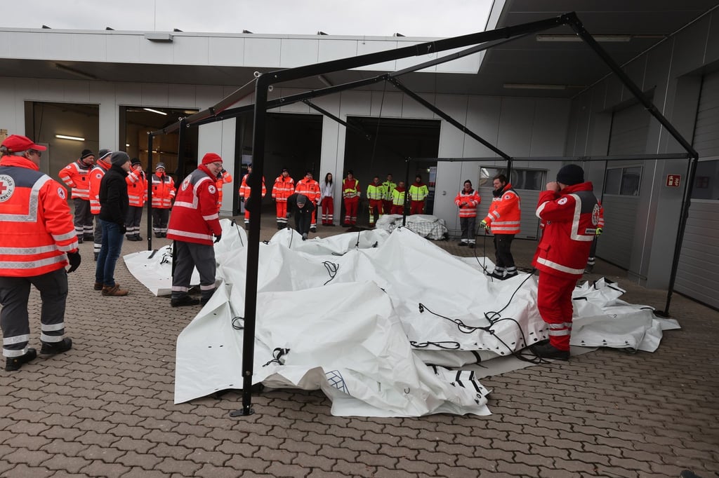 Mitglieder verschiedener Hilfsorganisationen stehen bei der Übergabe von modularen Zeltsystemen für den Katastrophenschutz auf einem Hof.