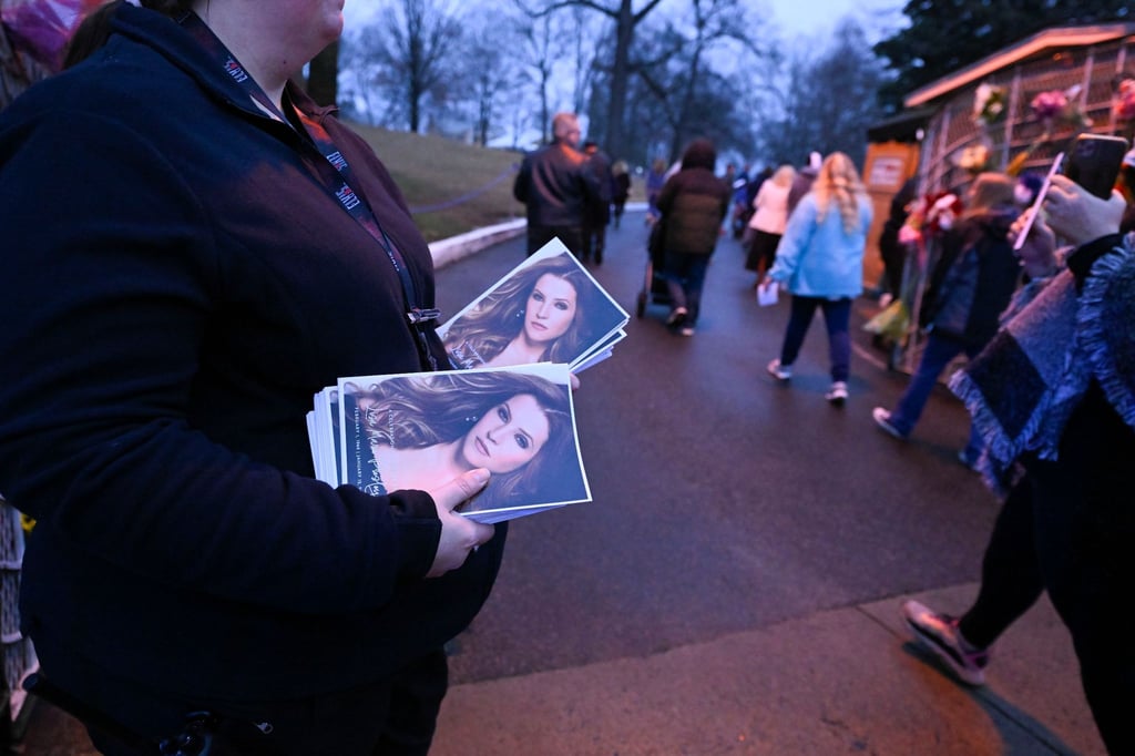Eine Frau hält Flyer mit einem Bild von Lisa Marie Presley, während Menschen an ihr vorbeigehen, um in Graceland an einem Gedenkgottesdienst teilzunehmen.