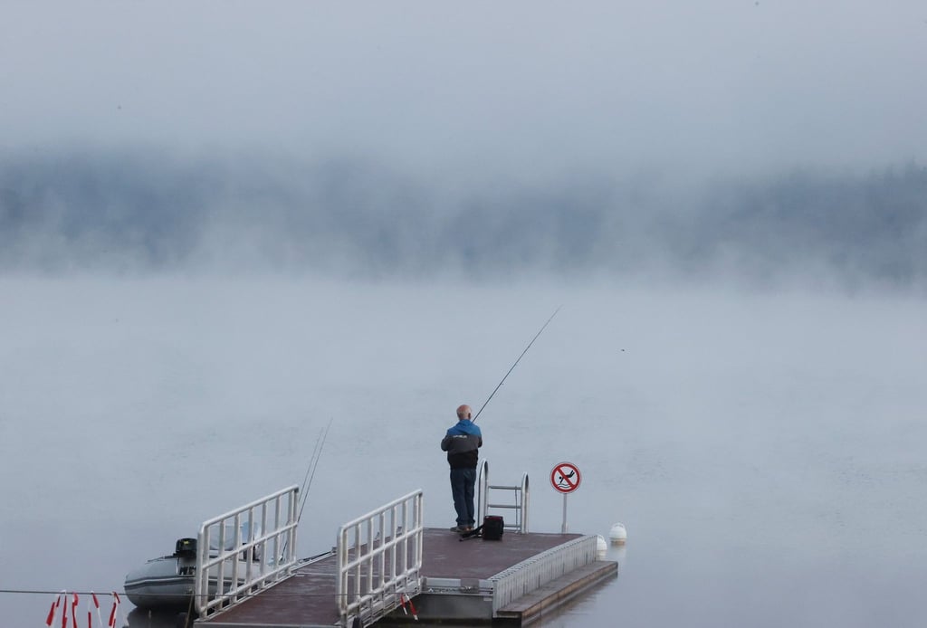 Ein Angler steht auf einem Steg am Ufer der Bleilochtalsperre in der Morgendämmerung.