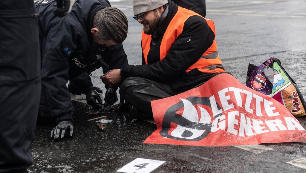 Ein Polizeibeamter versucht die festgeklebte Hand eines Demonstranten von der Halenseestraße zu lösen.