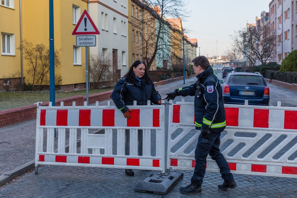 Einsatzkräfte des Ordnungsamtes der Stadt stellen an einer Straße Absperrungen auf.
