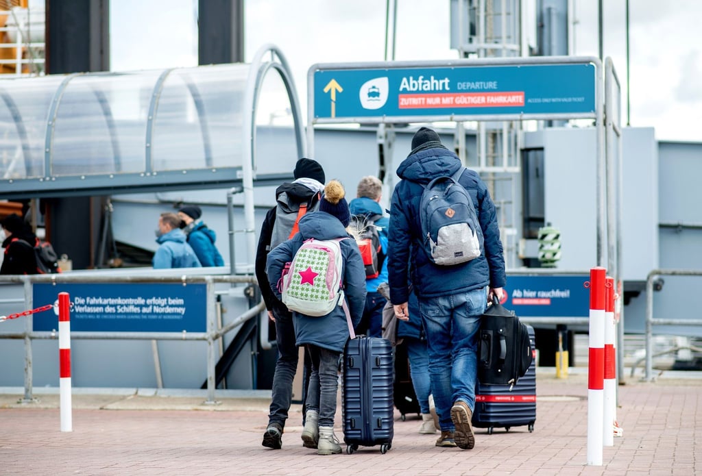 Touristen gehen am Fährterminal mit Gepäck zu einem Fährschiff der AG Reederei Norden-Frisia, um auf die Insel Norderney zu fahren.