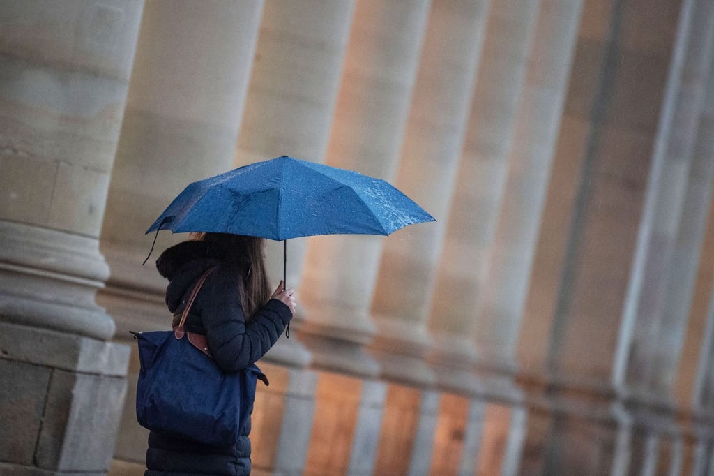 Eine Passantin geht bei Regen durch die Stadt.