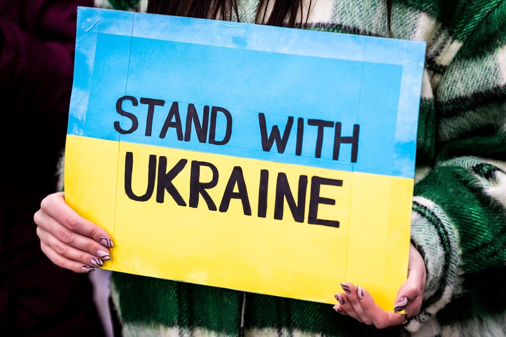 Der Schriftzug „Stand with Ukraine“ ist auf dem Plakat einer Demonstrantin zu lesen.