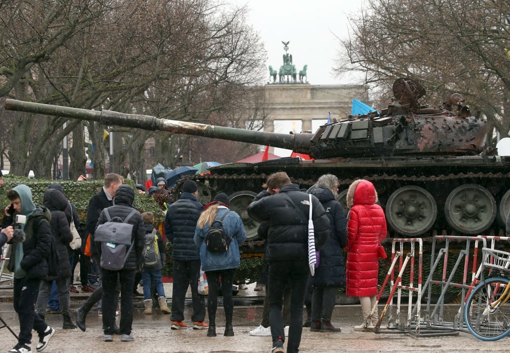 Passanten stehen vor einem in der Ukraine zerstörten russischen Panzer.
