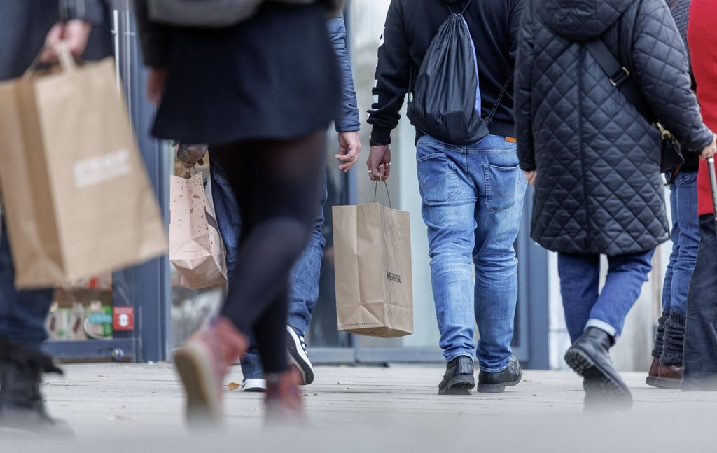 Menschen gehen mit ihren Einkaufstaschen auf einer Straße entlang.