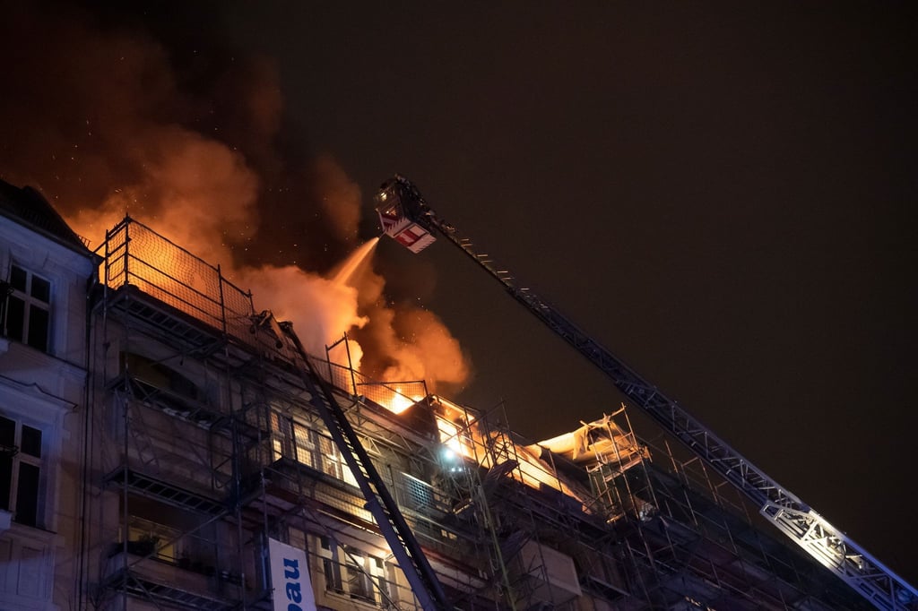 Ein Feuerwehrmann löscht von einer Drehleiter aus die Flammen auf dem Dach eines Wohnhauses.