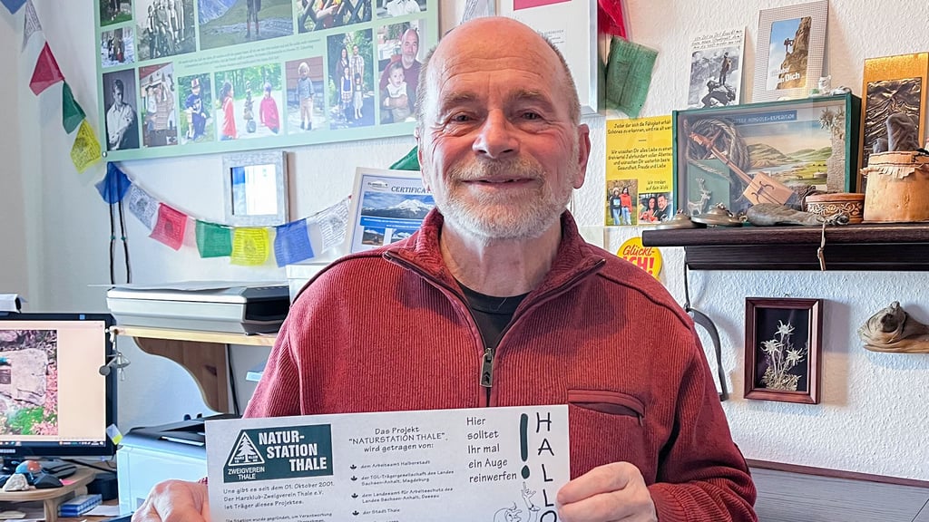 Horst Walther zeigt einen Flyer, den die Naturstation an Schulen verteilte. Im Hintergrund sind Andenken und Fotos von seinen Reisen zu sehen.