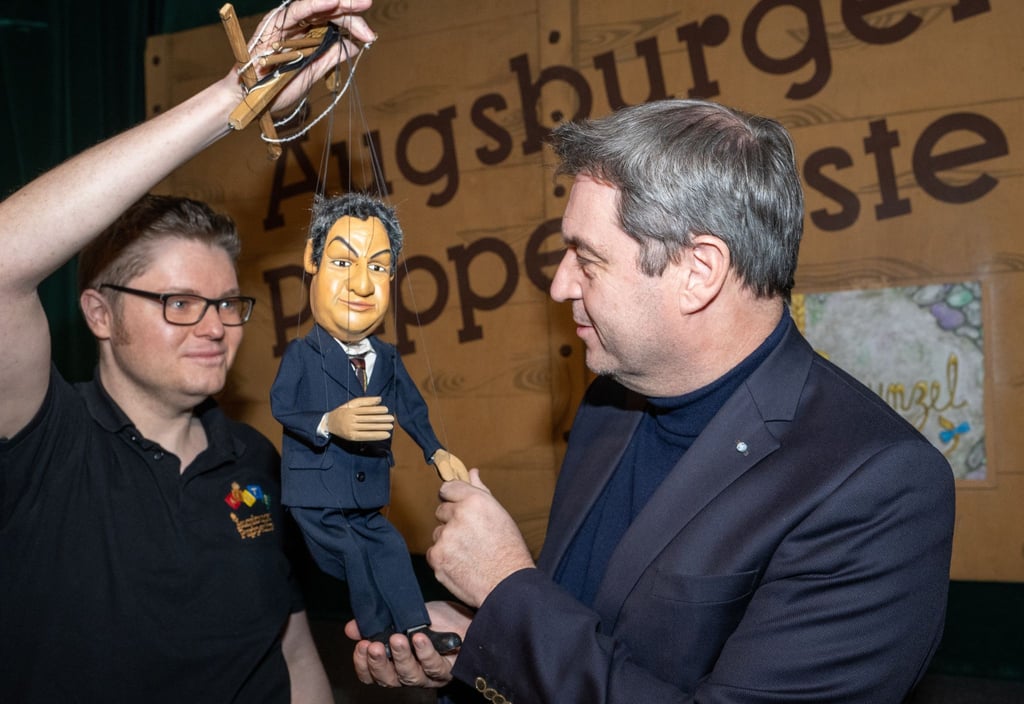 Markus Söder (r, CSU), Ministerpräsident von Bayern, gibt in der Augsburger Puppenkiste einer Söder-Marionette die Hand.