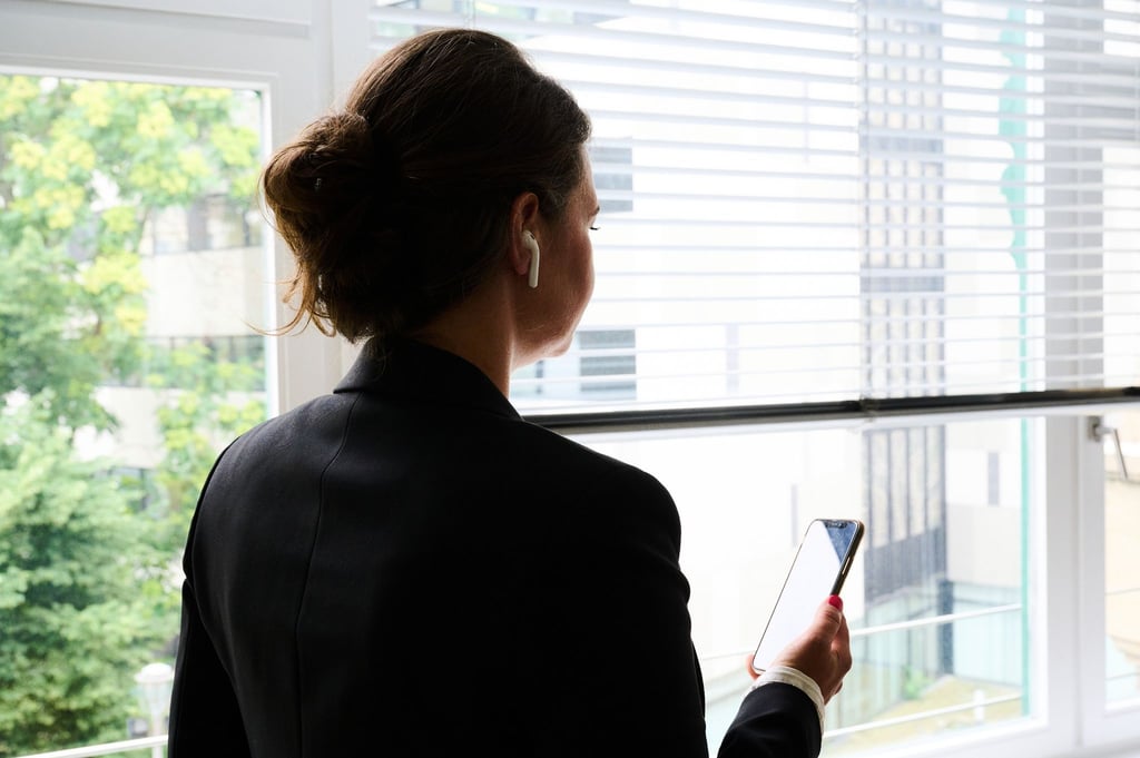 Eine Frau steht in einem Bürozimmer am Fenster und telefoniert über ein Headset.