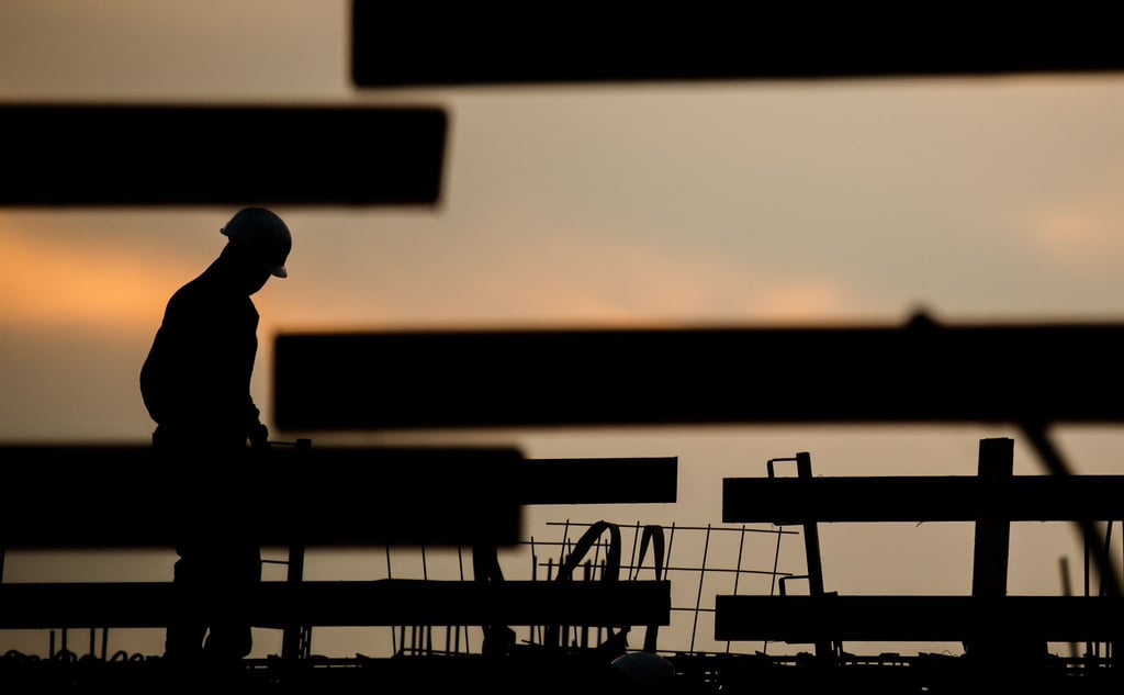 Die Silhouette eines Bauarbeiters zeichnet sich auf einer Baustelle vor dem Morgenhimmel ab.
