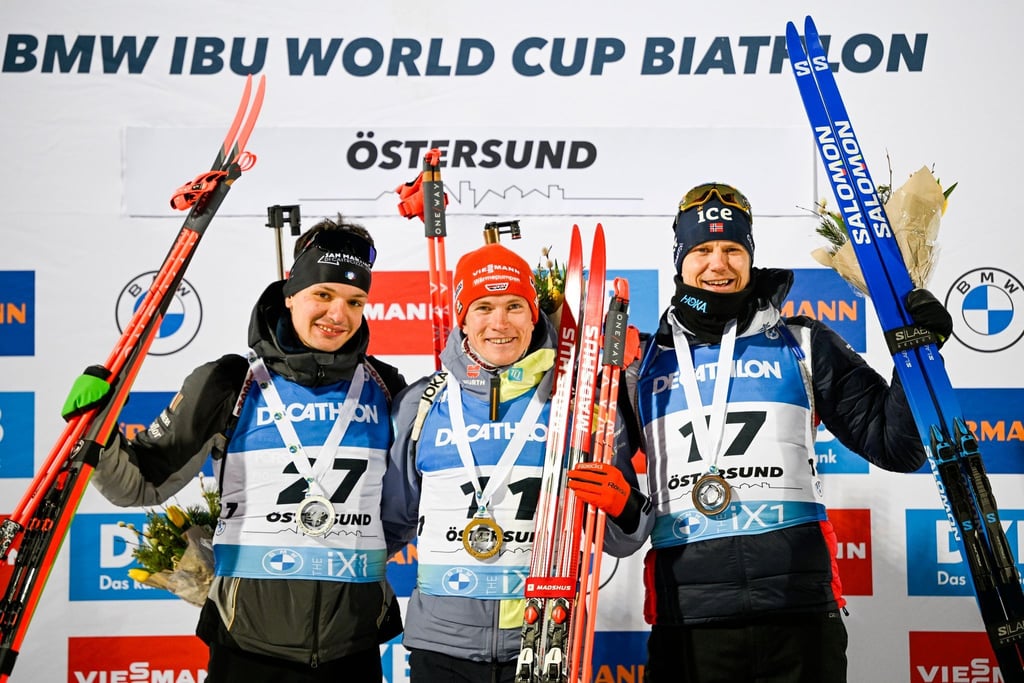 Benedikt Doll (M) feiert auf dem Podium seinen Sieg. Daneben: Tommaso Giacomel (l), Zweitplatzierter aus Italien, und Vetle Sjastad Christiansen, Drittplatzierter aus Schweden.
