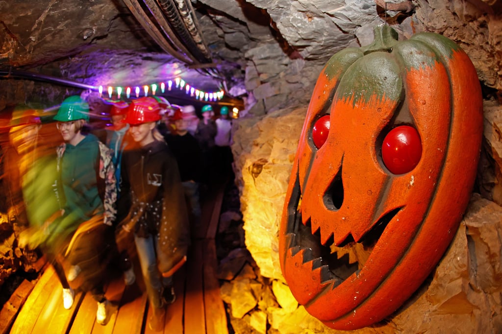 Besucher gehen durch den Stollen im Besucherbergwerk Röhrigschacht in Wettelrode an einem Kürbisgesicht vorbei (Wischeffekt durch Langzeitbelichtung). Es werden hier Halloween Führungen angeboten. Im Besucherstollen sind dafür gruselige Dekorationen verbaut worden. Die Gäste treffen auf Geister und andere Gestalten.