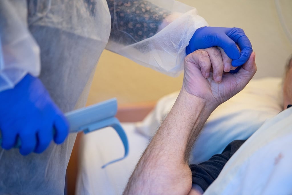 Eine Altenpflegerin im Schutzanzug hält die Hand eines Bewohners.