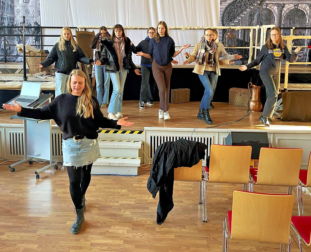 Schulkoordinatorin Carolin Kunze zeigt den Schülerinnen vor der Bühne in der Aula, wie sie sich richtig zur indischen Musik bewegen.