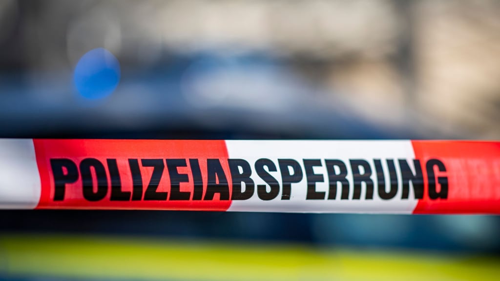 Ein Absperrband mit der Aufschrift „Polizeiabsperrung“ ist vor einem Polizeiwagen aufgespannt.