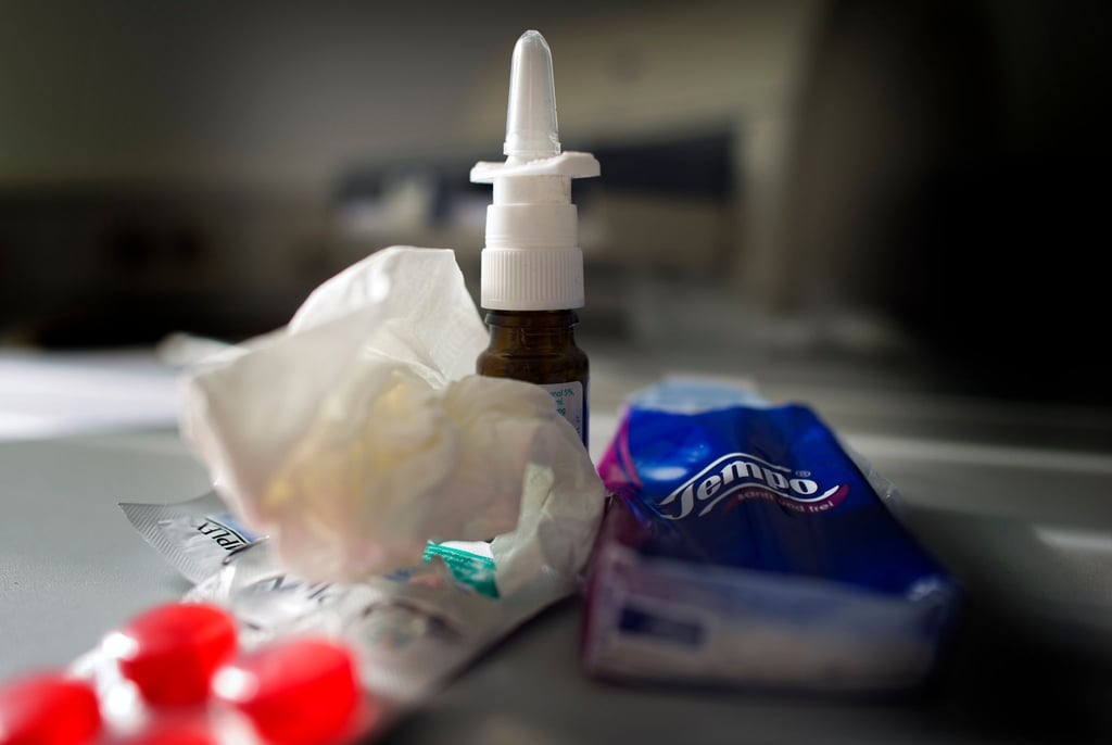 Anti-Erkältungsmittel wie Nasenspray, Halstabletten und Papiertaschentücher liegen auf einem Tisch.