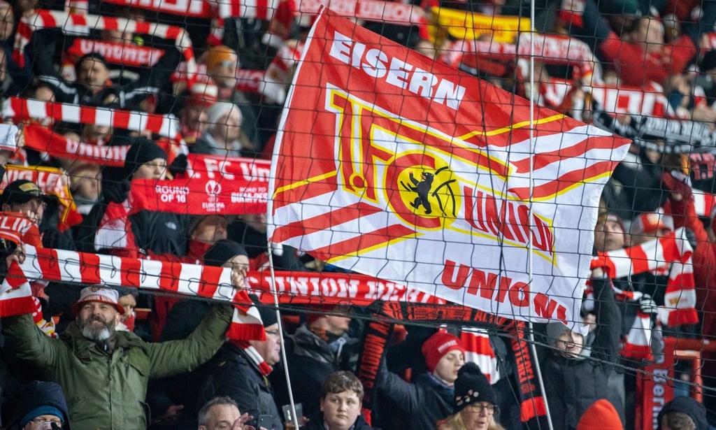 Fans von Union Berlin feuern ihr Team mit Schals und Fahnen an.