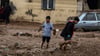 Kinder gehen nach heftigen Regenfällen eine schlammige Straße in Sanliurfa entlang.